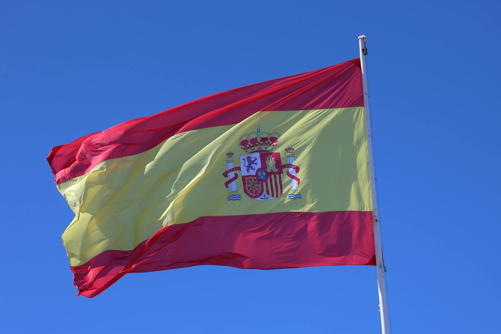Vibrant Spanish flag waving in Cádiz, Spain, set against a bright blue sky.