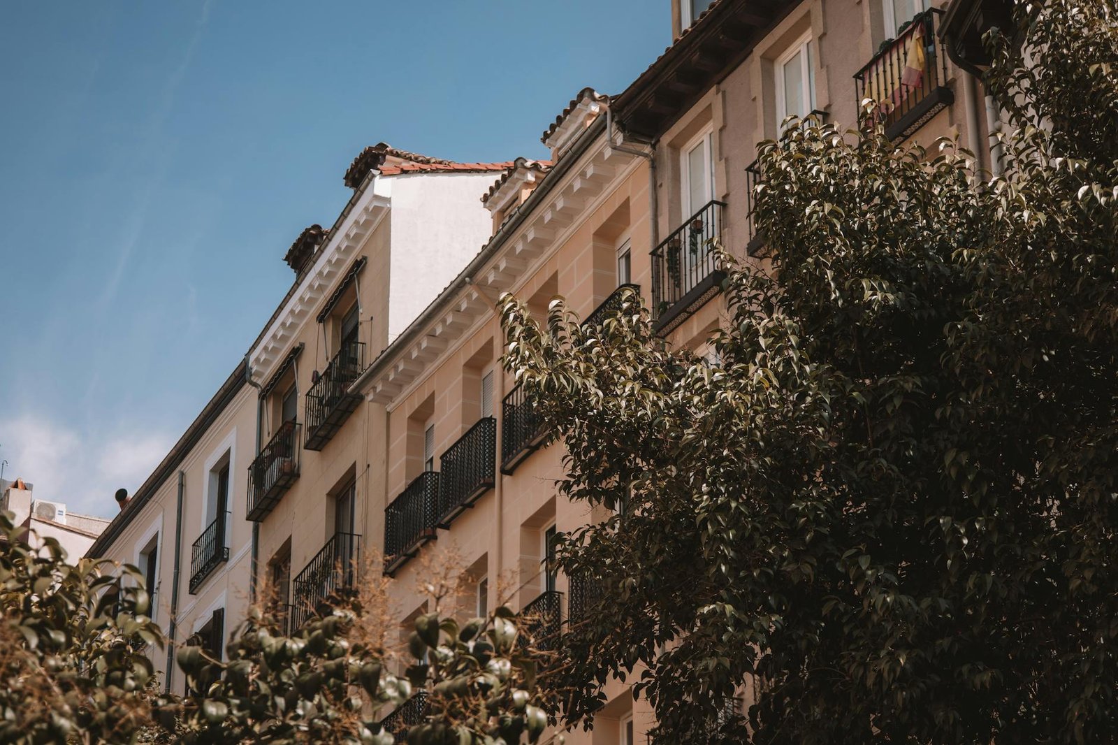 Elegant residential building with balconies and lush trees in Madrid, Spain.