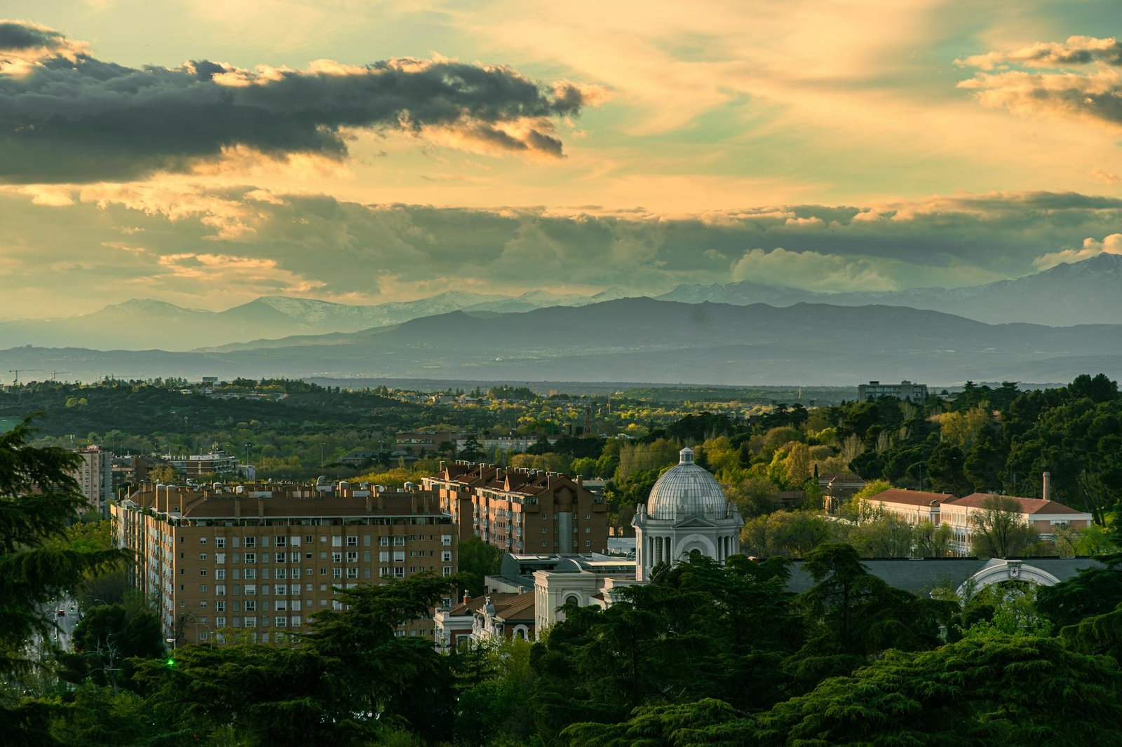 Panoramic view of Madrid's urban landscape with mountains and a dramatic sky at dusk.