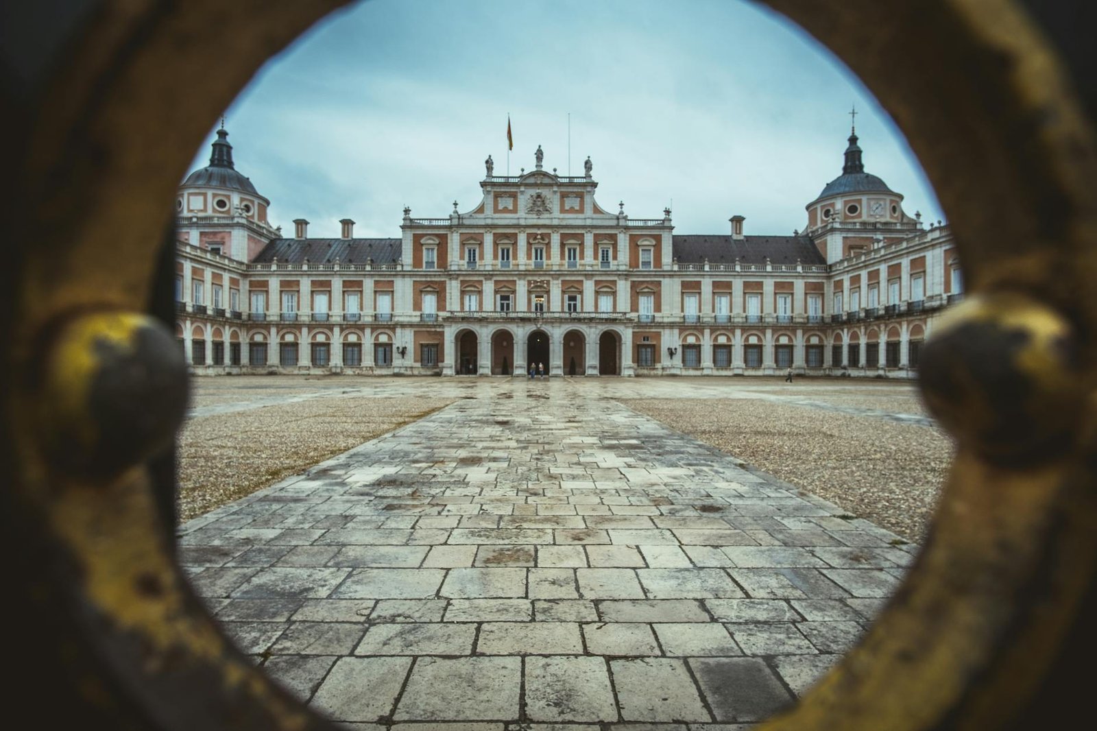 View of the Royal Palace of Aranjuez in Spain through an ornate gate. Historic architecture in a regal setting.