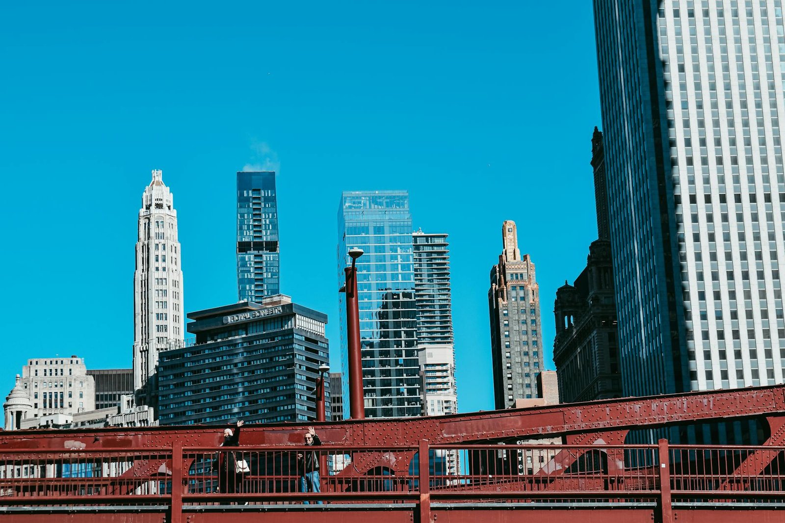 Explore Chicago's skyline featuring modern skyscrapers and a red steel bridge under a clear blue sky.